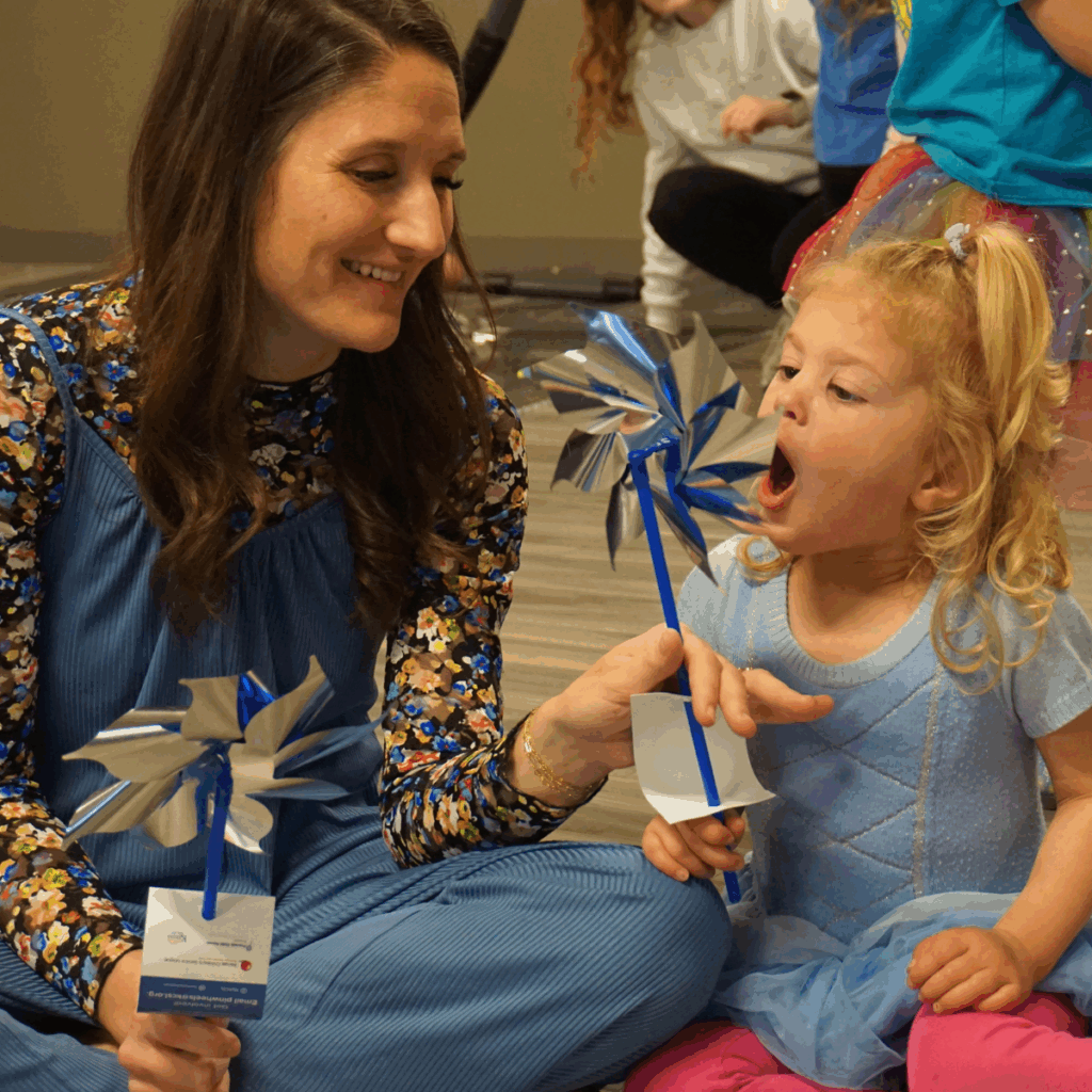 teacher holding pinwheel for young student, student taking a breath to blow pinwheel