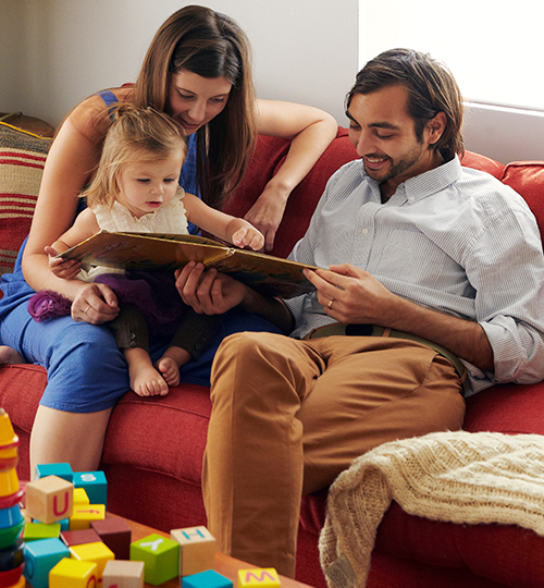 parents reading to daughter in living room